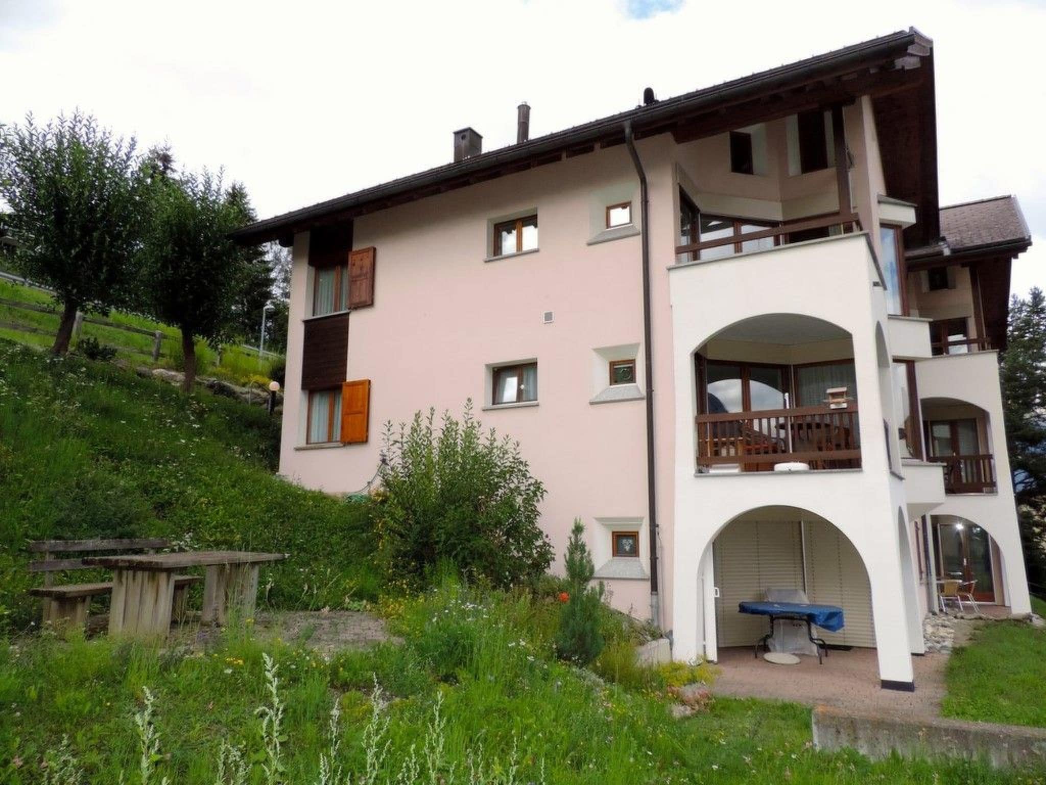 Ein zweigeschossiges Gebäude mit einem Balkon im oberen Geschoss, einer Garagentür im Erdgeschoss und einer kleinen Außen-Sitzgelegenheit.