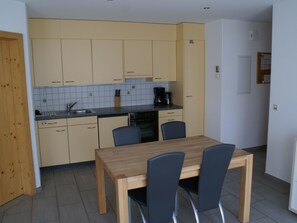 Eine kompakte Küche mit Esstisch und Stühlen, einer Kaffeemaschine und einem Geschirrspüler.