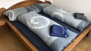 Un lit avec une tête de lit en bois, des oreillers à motifs gris et blancs, et une serviette bleue pliée posée sur le lit.