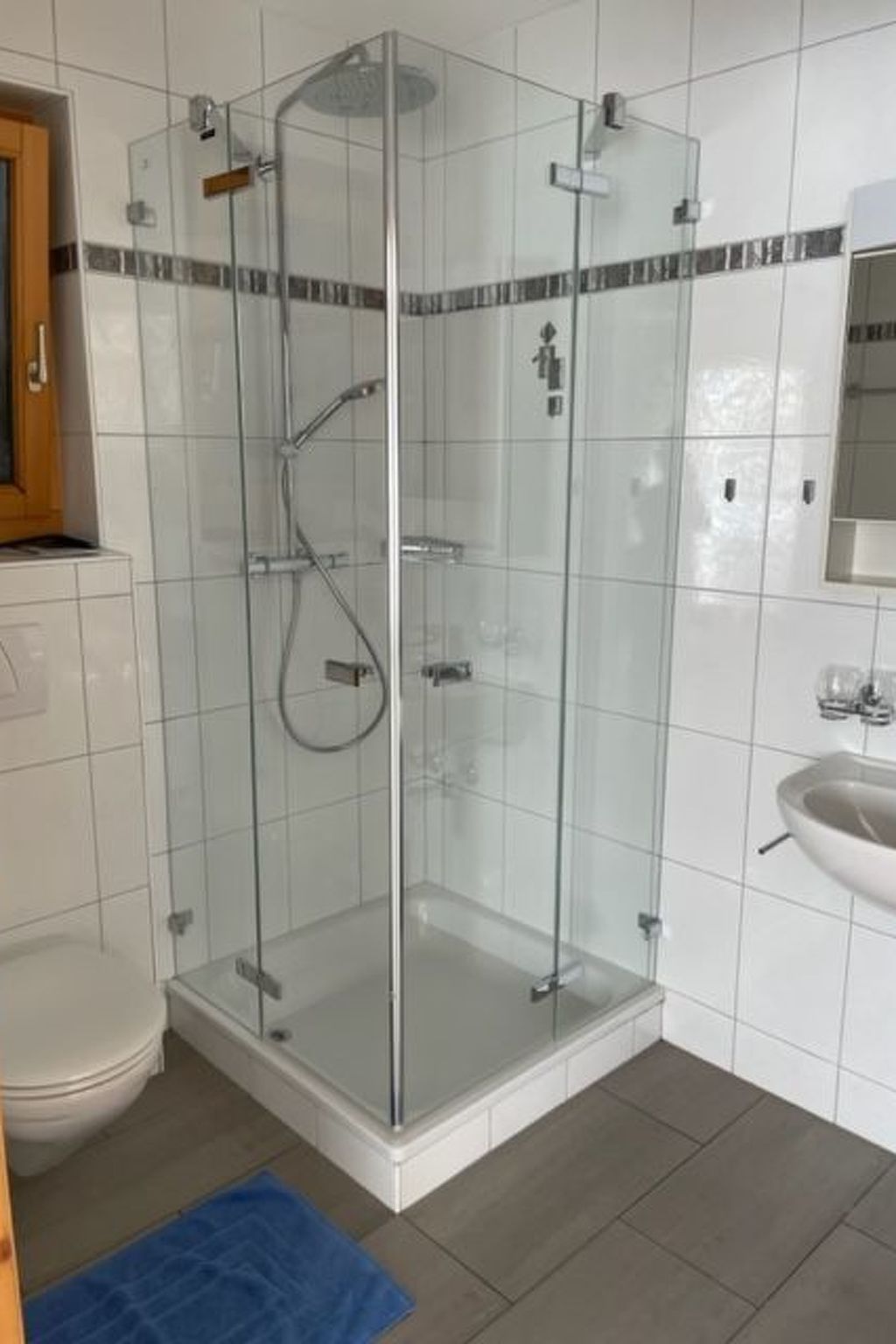 Ein modernes Badezimmer mit einer gläsernen Duschkabine, einem weißen Waschbecken und einem gefliesten Boden.