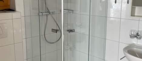 Un bagno moderno con doccia vetro, lavandino bianco e pavimento piastrellato.