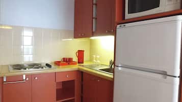 Una cocina con armarios rojos, un refrigerador blanco, un microondas, un fregadero y una estufa.