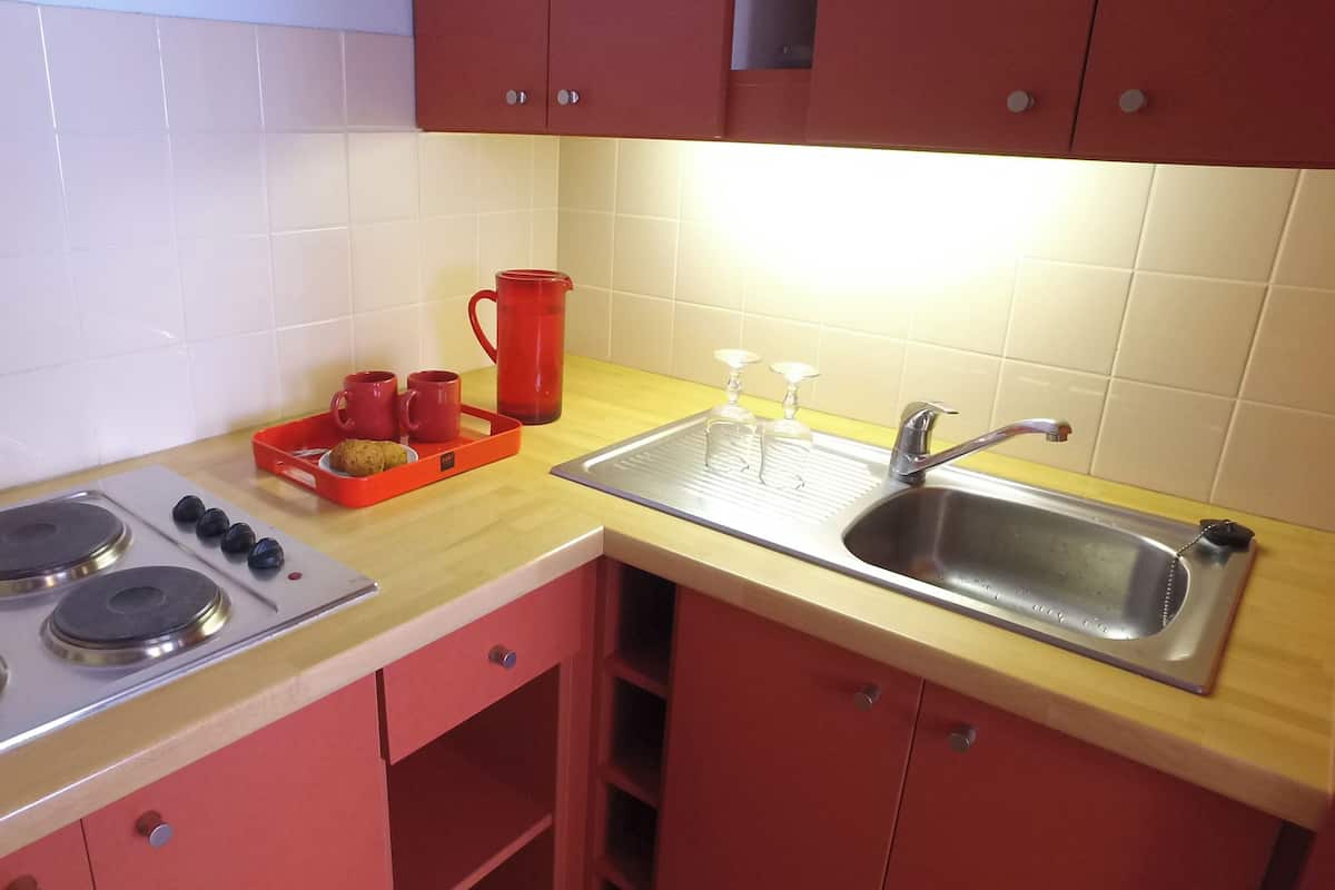 A kitchen with a stove, sink, and red cabinets.