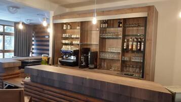 A bar area with a wooden counter, shelves with glasses and bottles, and a coffee machine.