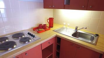 Una cocina con estufa, lavamanos y armarios rojos.