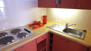 A kitchen with a stove, sink, and red cabinets. - Vvf Villages Prapoutel (Les Adrets)