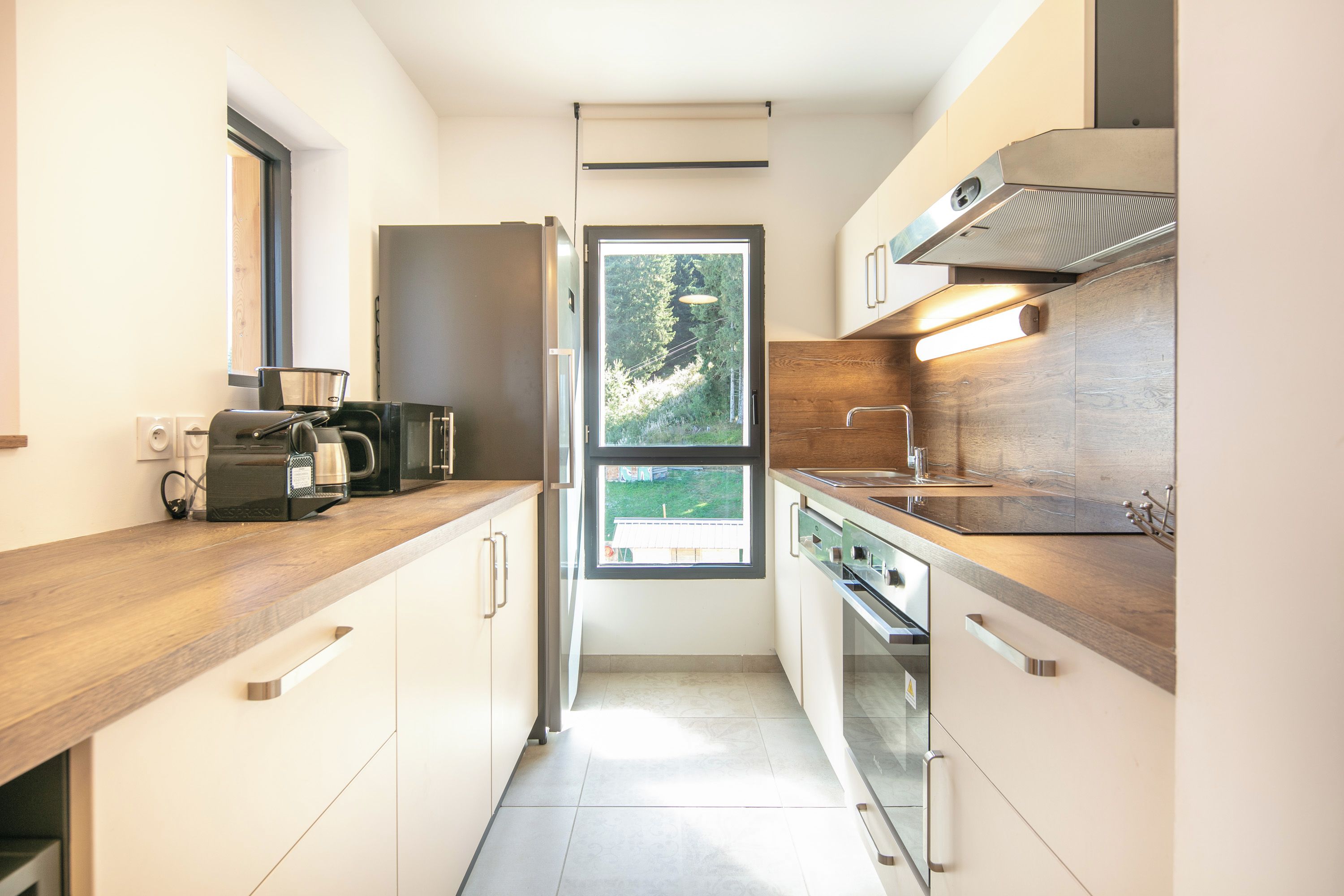 Una cocina moderna con encimera de madera, electrodomésticos de acero inoxidable y una ventana que ofrece vistas al verdor exterior.