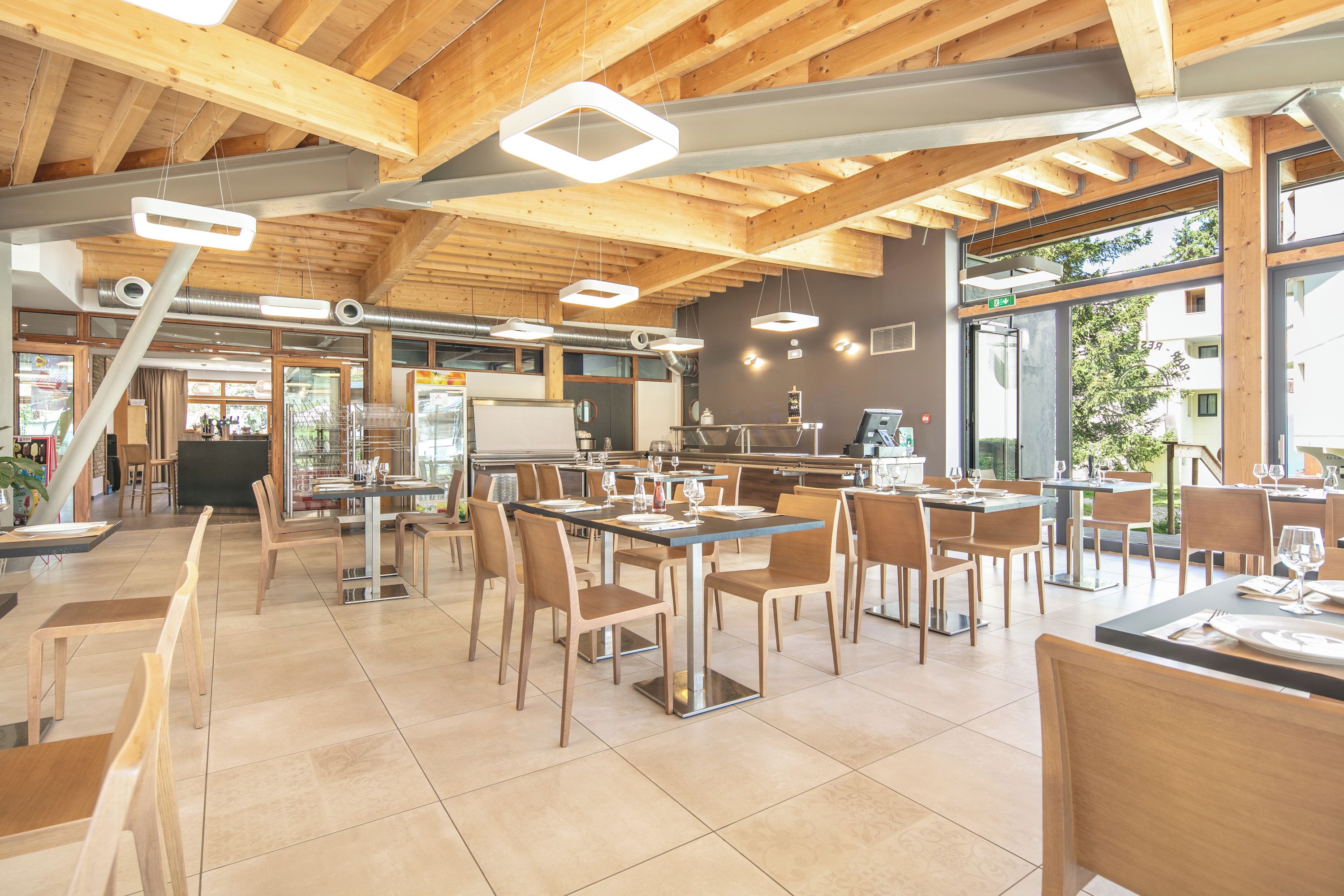 Un restaurante espacioso con vigas de madera, iluminación moderna y grandes ventanales que ofrecen vistas al exterior.
