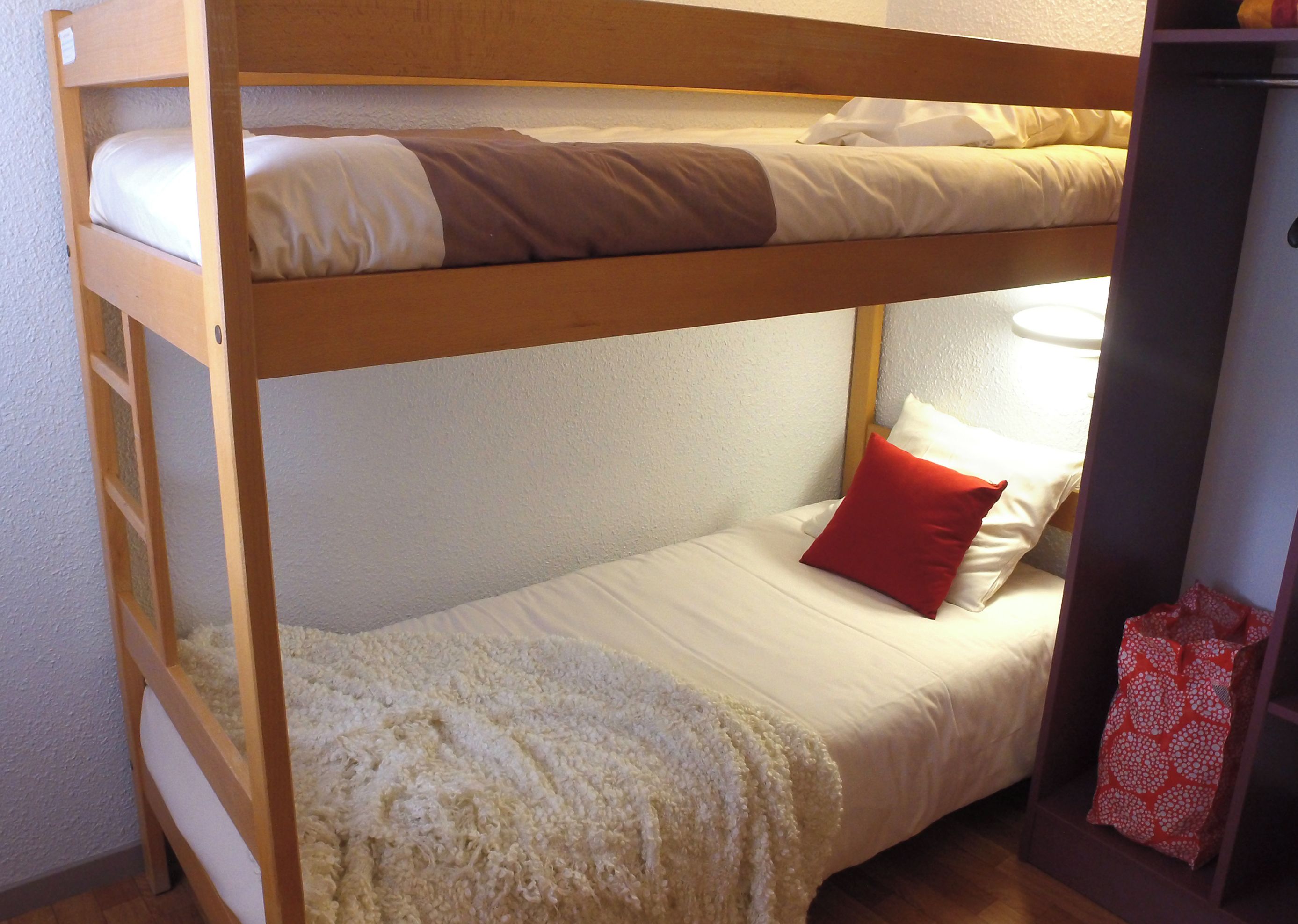 A bunk bed with a lower bunk, a white blanket, a red pillow, and a wooden ladder.