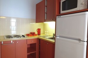 A kitchen with red cabinets, a white refrigerator, a microwave, a sink, and a stove. - Vvf Villages Prapoutel (Les Adrets)