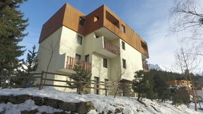 A multi-story building with balconies, a stone wall, and snow-covered ground. - Vvf Villages Prapoutel (Les Adrets)