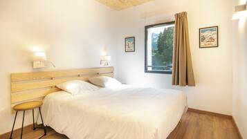 Un dormitorio con cabecera de madera, cama individual, mesita de noche, ventana con cortinas y dos luces fijadas a la pared.