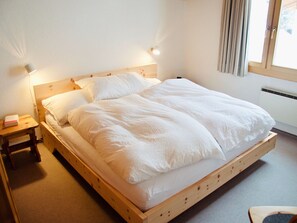 A single-bed room with a wooden frame, white bedding, a bedside table with a lamp, and a window with curtains. - Hideaway in Scuol, (Scuol) by Interhome (Scuol)