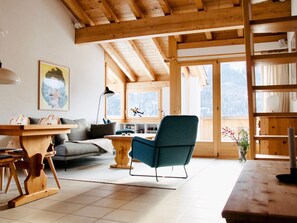 Ein gemütliches Wohnzimmer mit Holzboden, einer Couch, einem blauen Sessel, einem Holztisch und einem Bücherregal.