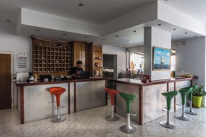 A bar area with a bartender, a shelf with bottles, and a painting on the wall. - Vossos (Zakynthos)
