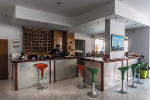 Zona de bar con un cantinero, repisas con botellas y un cuadro en la pared.