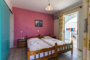 Un dormitorio con dos camas de madera, una mesita de noche, un estante en la pared y un cuadro.
