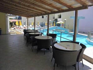 A covered outdoor area with a pool, lounge chairs, and tables. - Vossos (Zakynthos)