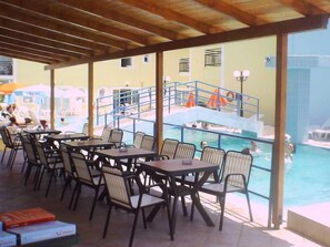 Un área de piscina al aire libre con mesas y sillas, un espacio de estar cubierto y vistas a la piscina.