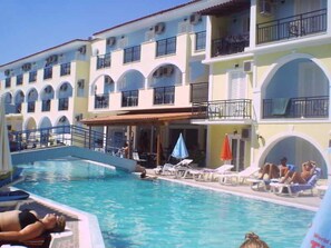 A hotel with a swimming pool, multiple balconies, and a covered area with lounge chairs. - Vossos (Zakynthos)
