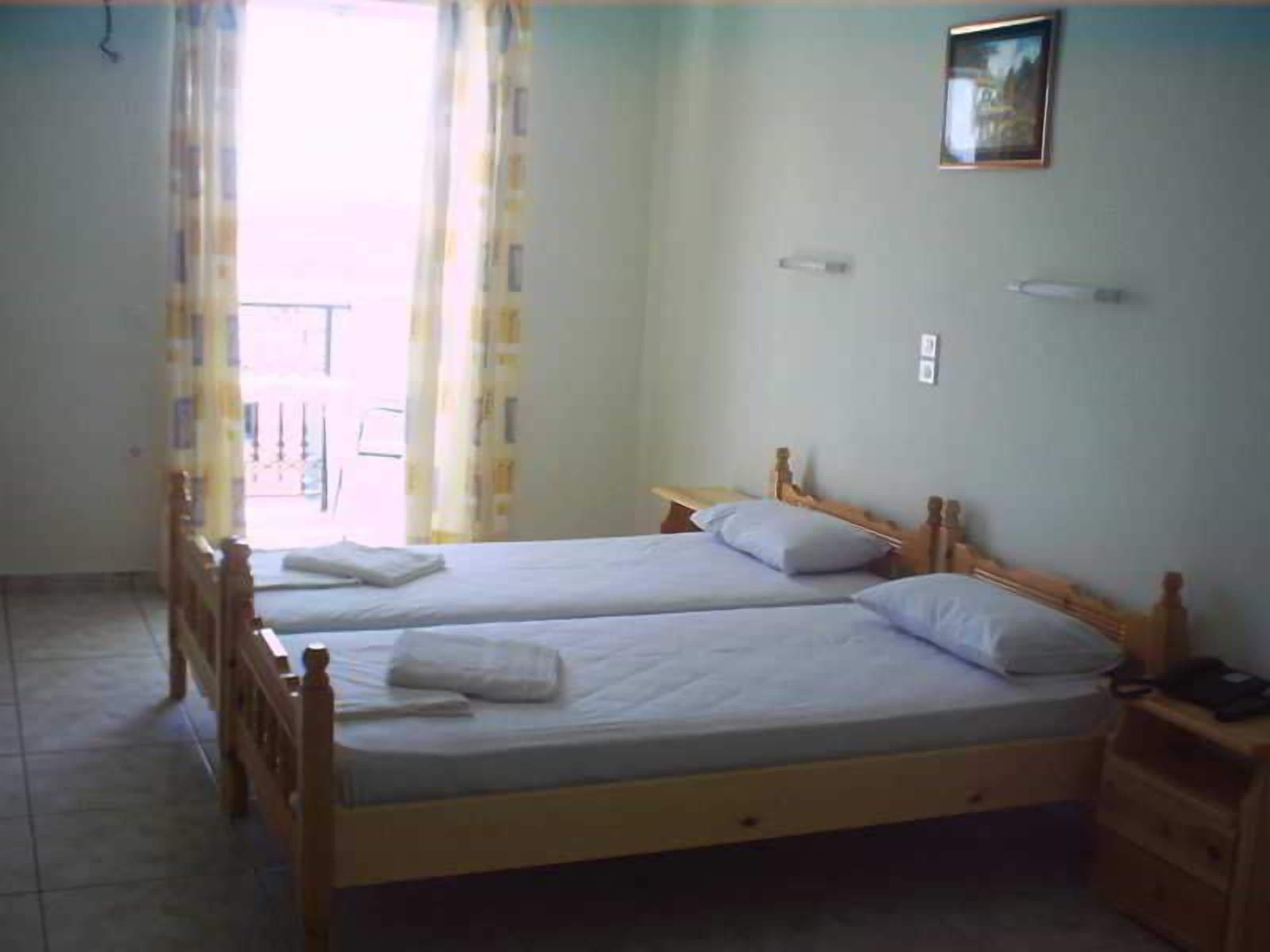 Ein Zimmer mit zwei Holzbett, einem kleinen Nachttisch, einem Stuhl und einem Fenster mit Vorhängen.