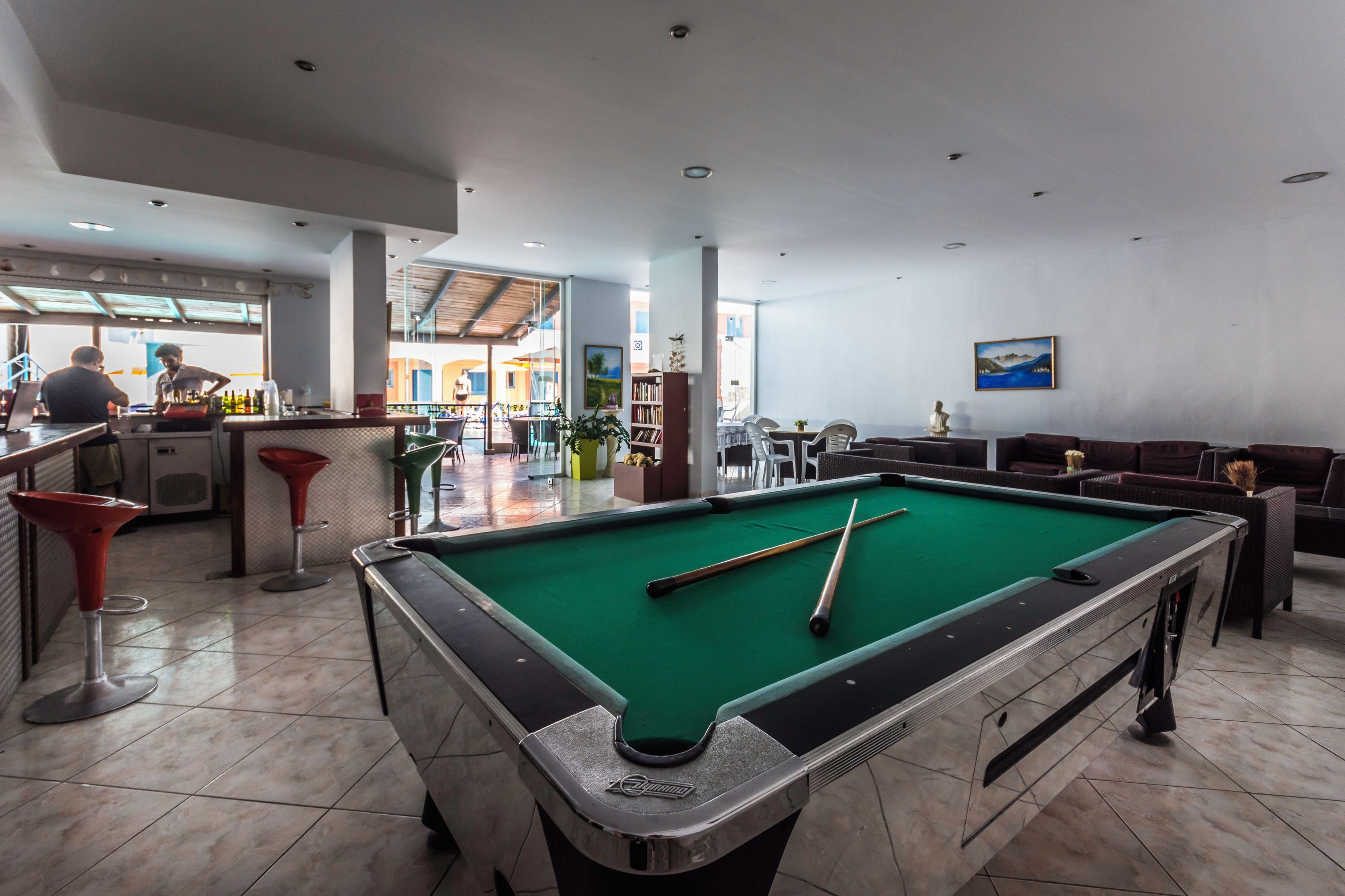 A pool table with pool cues, a bar area, and a seating area with a view of the outside.