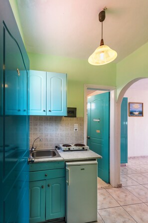 Una cocina con armarios azul verdoso, un lavamanos, una estufa y un refrigerador pequeño.