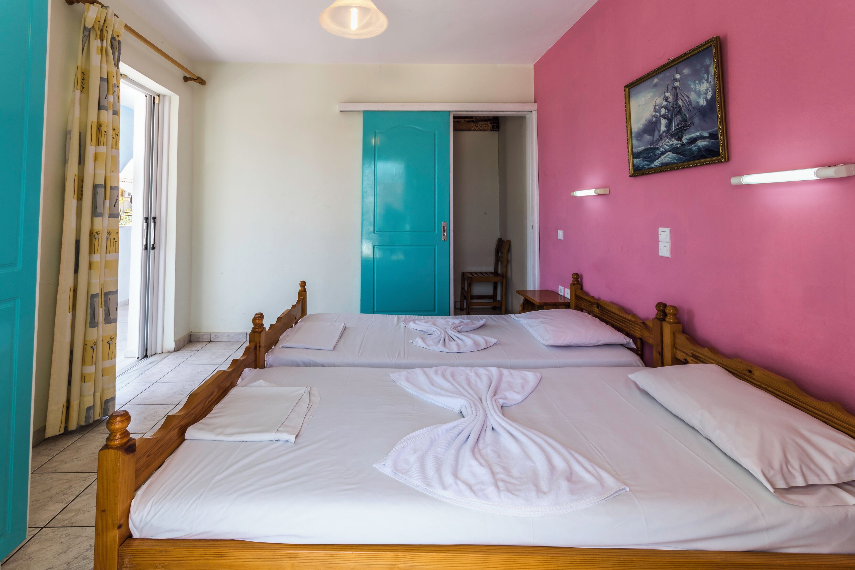 Hotellihuone, jossa on kaksi sänkyä, sininen ovi, seinällä taulu ja tuoli nurkassa.