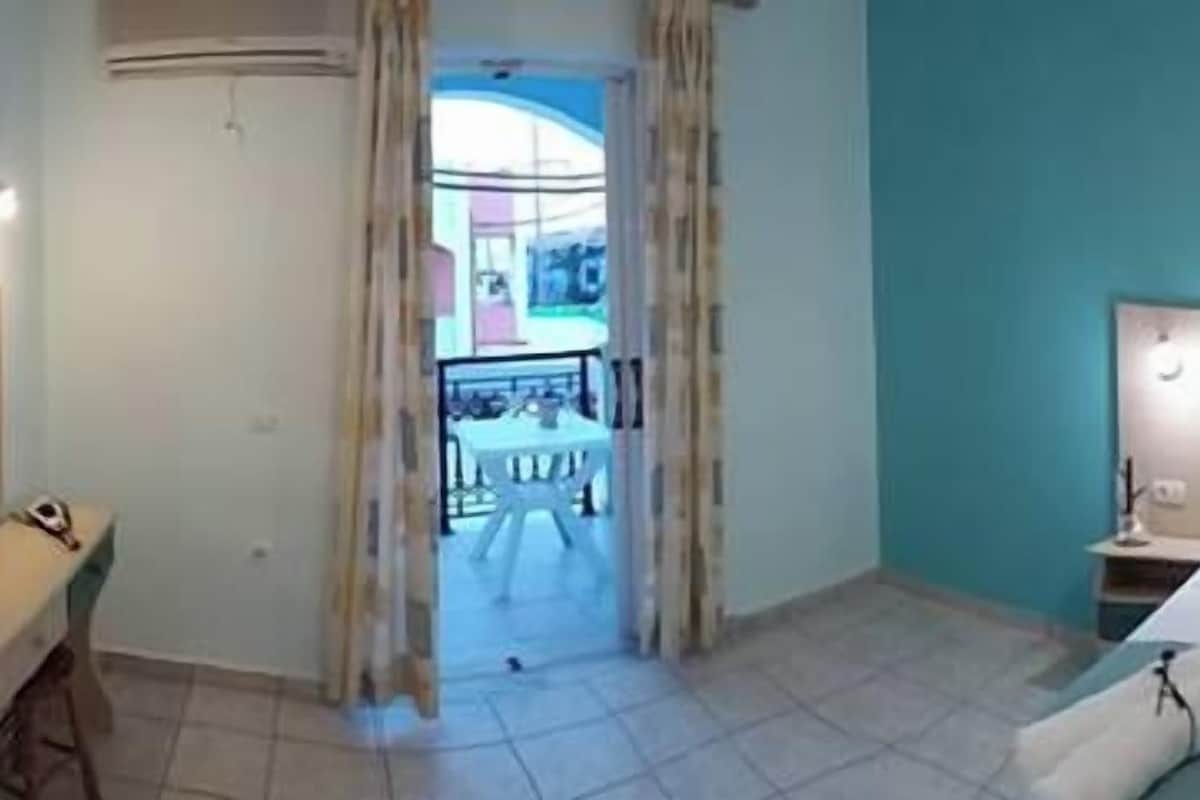 Habitación de hotel con una cama grande, una cama más pequeña, un escritorio y una silla. Hay un cuadro en la pared y una ventana con vistas al exterior.