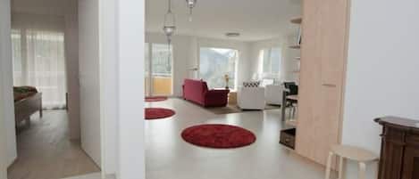 An open-plan living space with a kitchen area, a dining table, and a red circular rug.