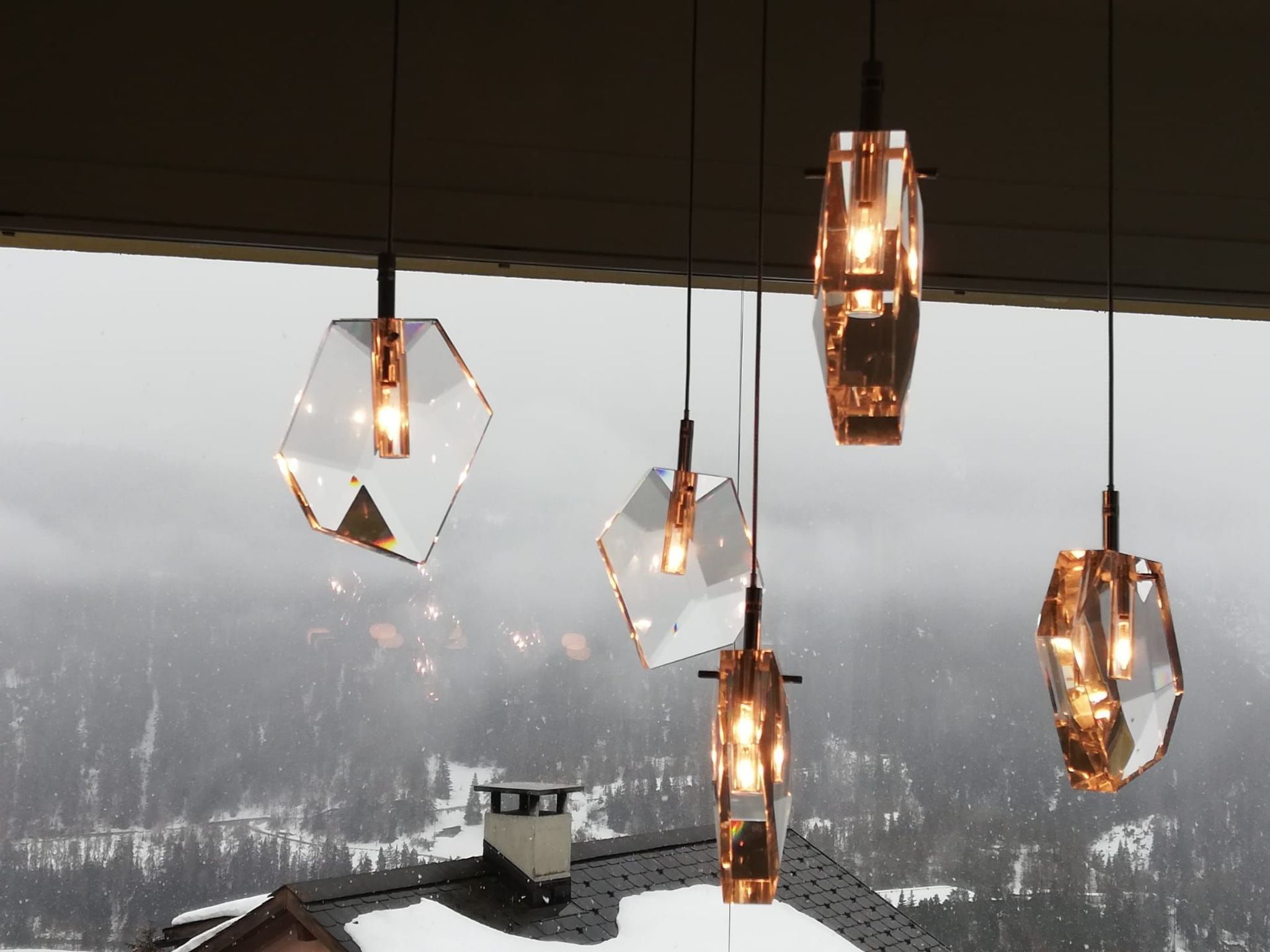 Una composizione di lampade pendenti geometriche, rifinite in rame, sospese al soffitto.