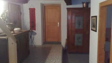 Un couloir étroit avec une porte en bois, une petite table avec une chaise et une décoration rouge suspendue.