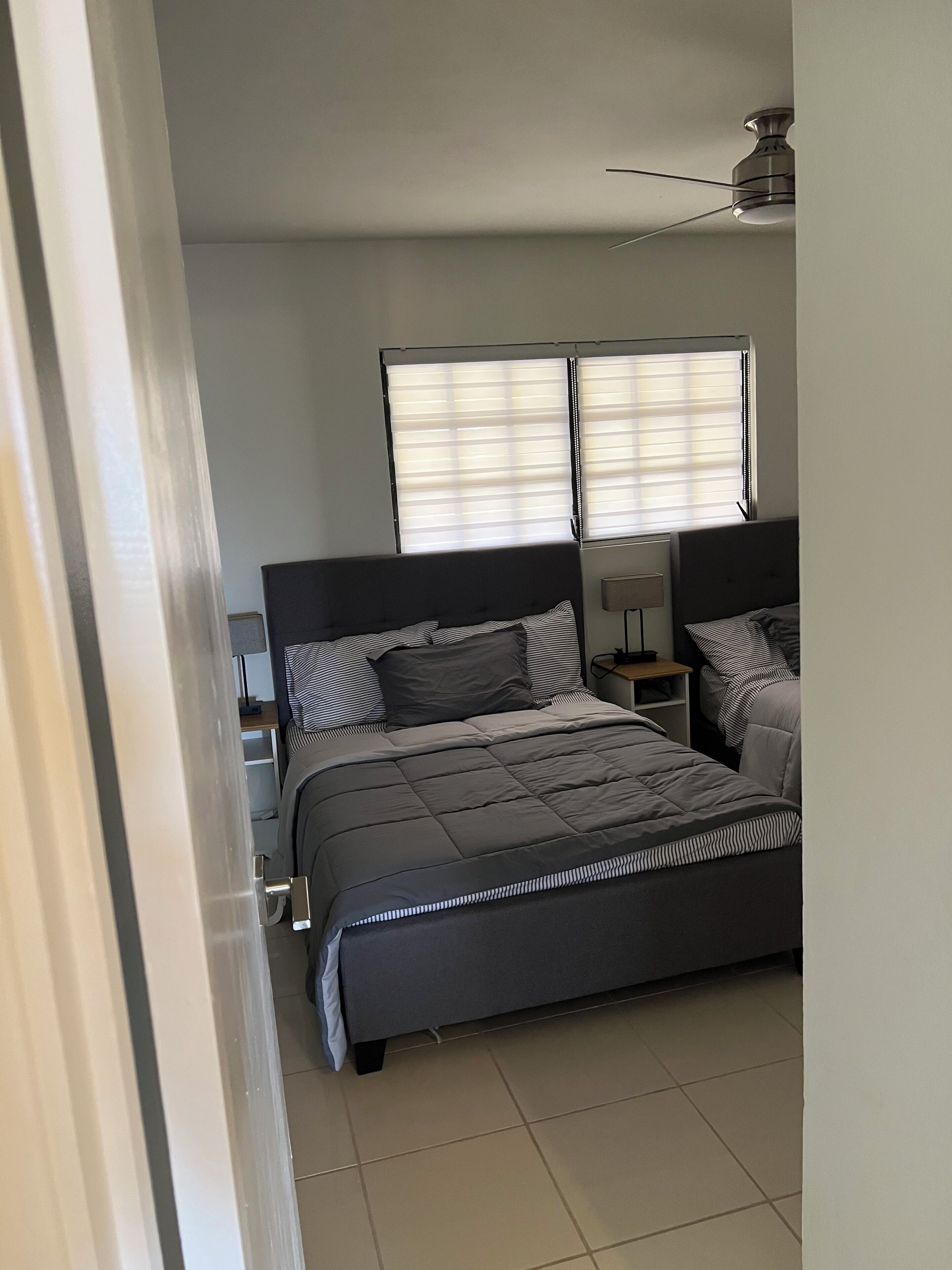 A bedroom with a bed, two bedside tables, a ceiling fan, and a window with blinds.