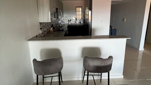 Une cuisine moderne dotée d’un îlot central, de deux tabourets de bar et donnant sur l’espace repas.