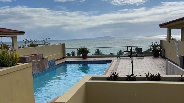 Une piscine avec vue sur la mer, un patio couvert et des plantes en pot.