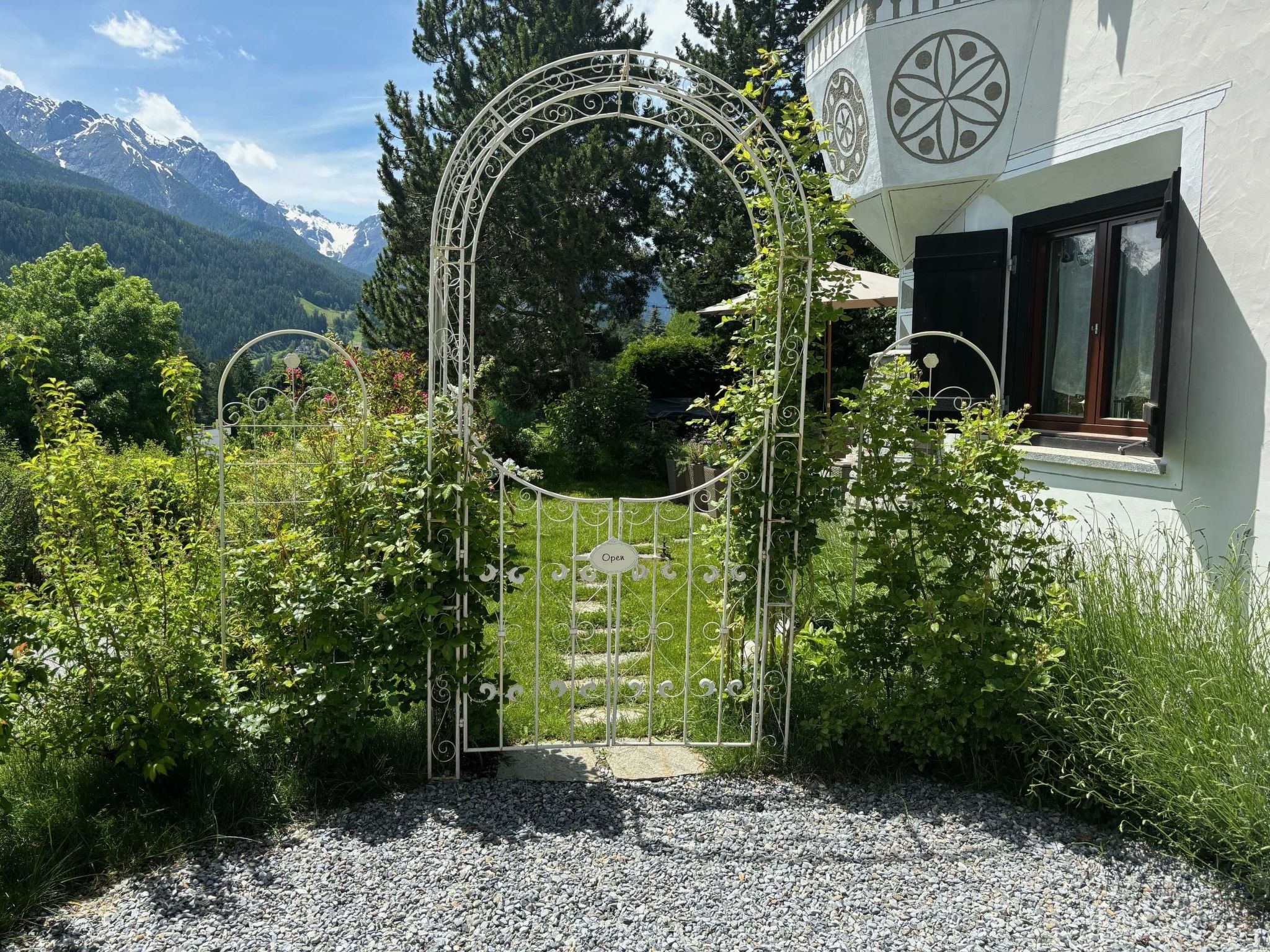 A gated entrance with a decorative archway, surrounded by lush greenery and a mountainous backdrop.