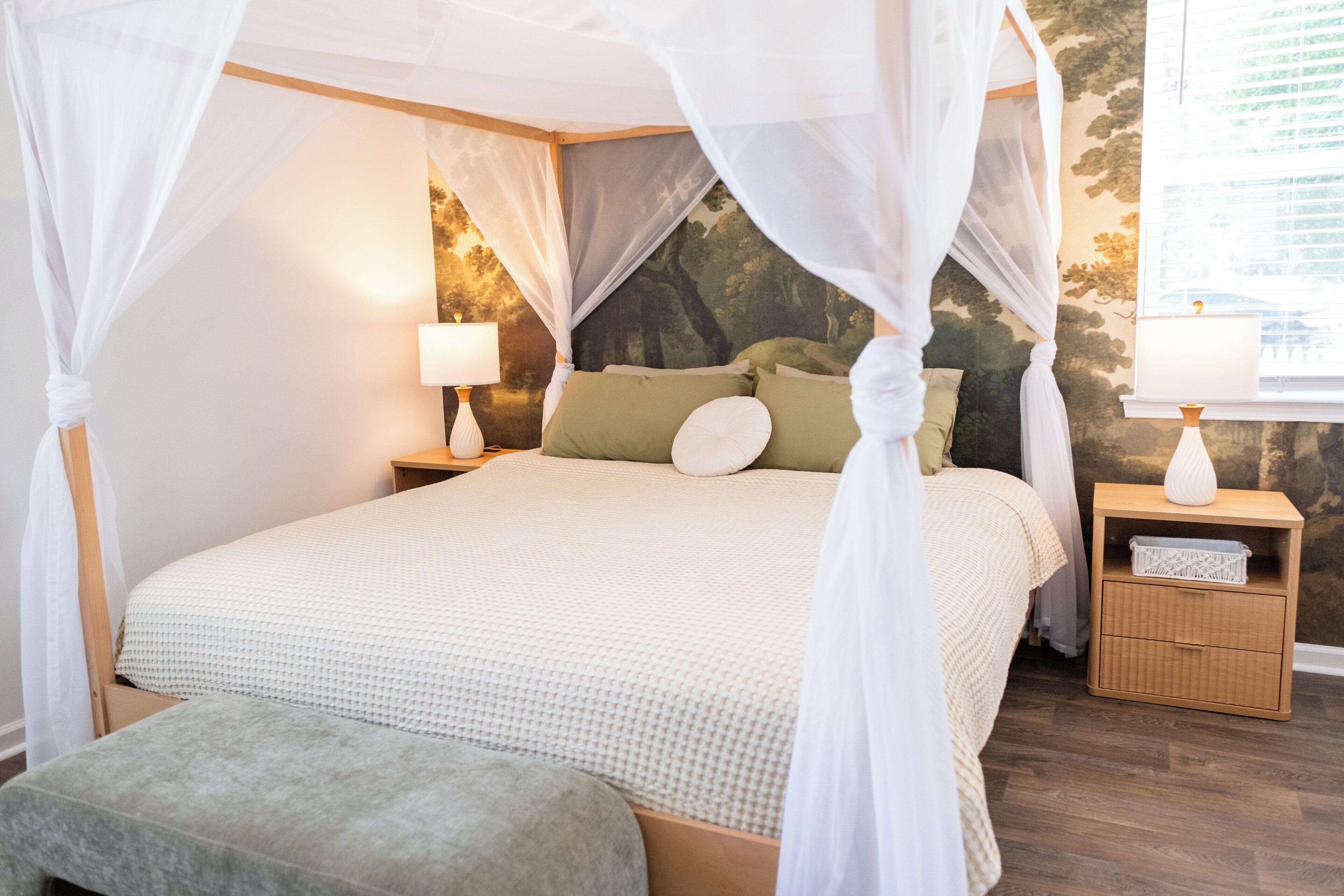 A bedroom with a canopy bed, a nightstand with a lamp, and a wall mural.