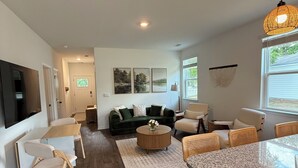 A modern living room with a dark green sofa, a round coffee table, and a kitchen area with a granite countertop and wicker chairs. - 3-bedroom house in fabulous Summerton next to lake (Summerton)