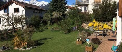 A residential area with a well-maintained lawn, a variety of flowering plants, and a view of snow-capped mountains in the background.