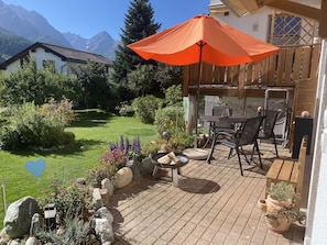 Une terrasse avec une table et des chaises, une clôture en bois et un jardin agrémenté de diverses plantes, ainsi qu’un panneau en forme de cœur.