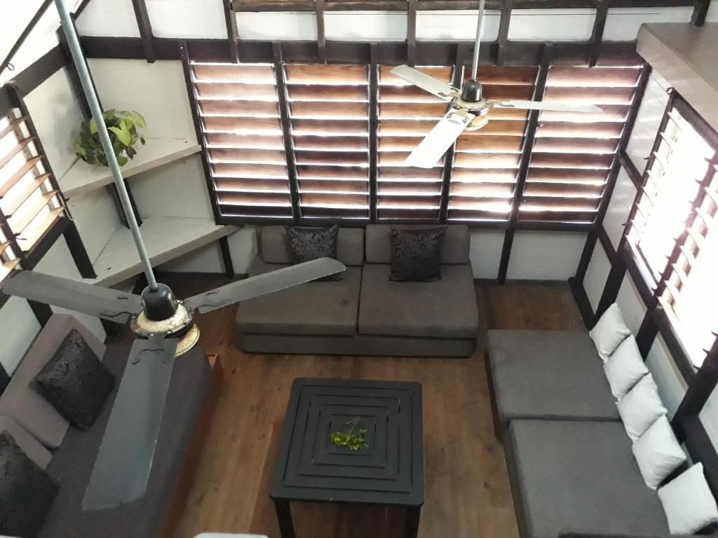 A room with a sofa, a small table, a ceiling fan, and a window with blinds.