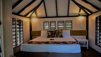 A bedroom with a large bed, wooden beams on the ceiling, a nightstand, and a window with a view.