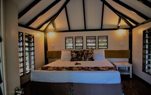 Quarto com uma cama grande, vigas de madeira no teto, mesa de cabeceira e janela com vista.