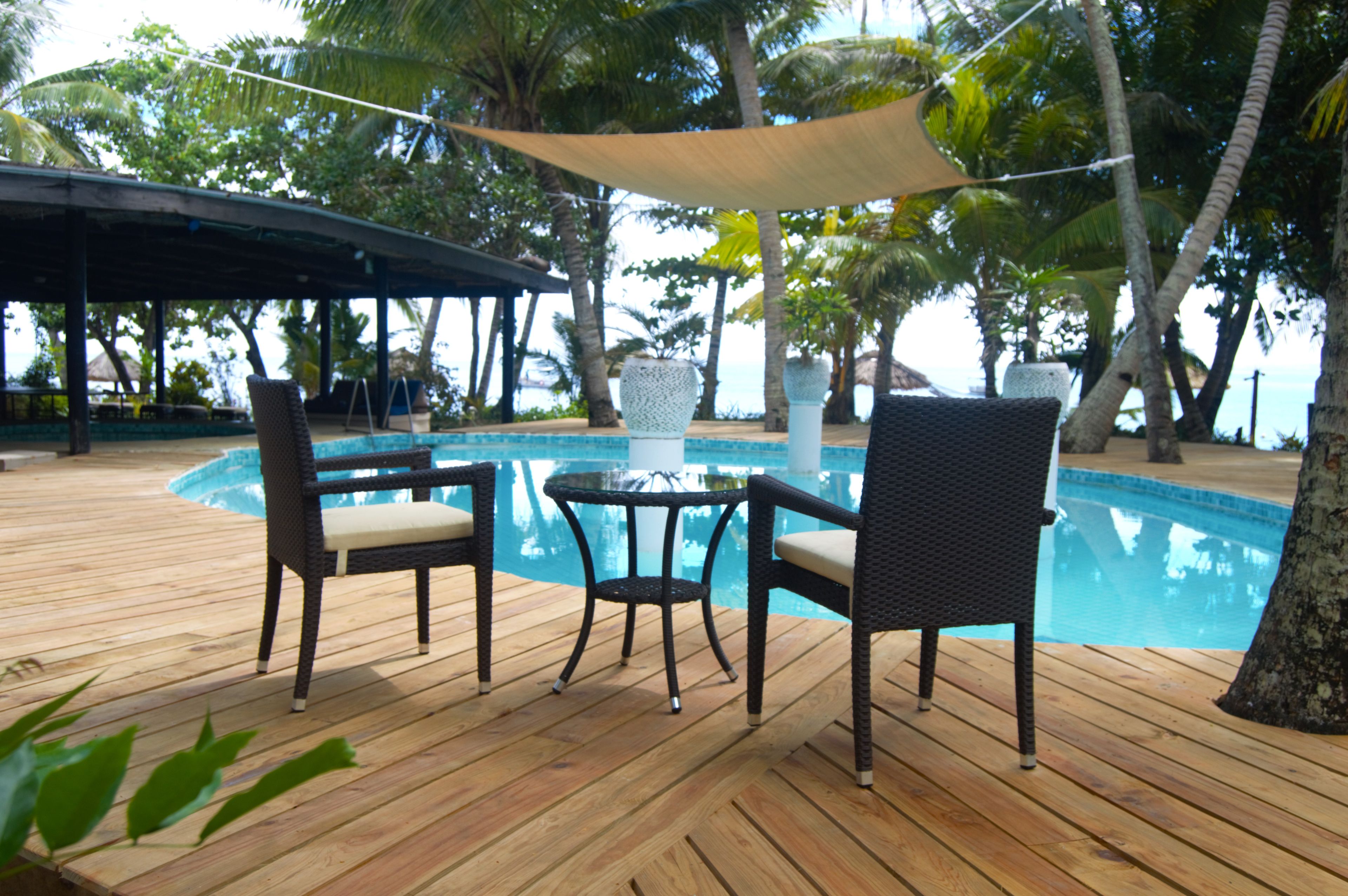 A wooden deck with a pool, wicker chairs, and a table.
