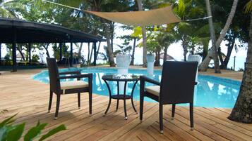 A wooden deck with a pool, wicker chairs, and a table.