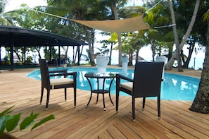 A wooden deck with a pool, wicker chairs, and a table.