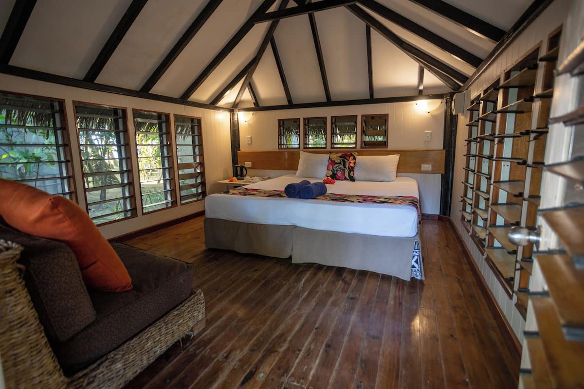 Ein Schlafzimmer mit einem großen Bett, Holzboden und Blick durch die Fenster.