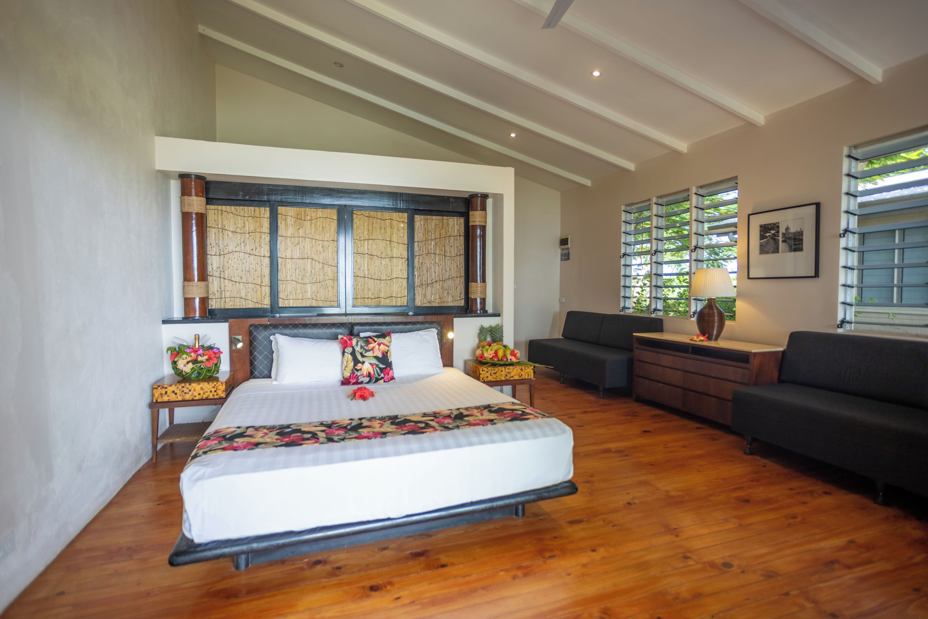 A spacious hotel room with a large bed, a sofa, a desk, and a window with blinds.