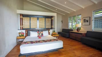 A spacious hotel room with a large bed, a sofa, a desk, and a window with blinds.