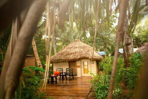 A thatched-roof hut with a wooden deck and outdoor seating area surrounded by lush tropical vegetation. - Likuri Island Resort Fiji (Lomowai)